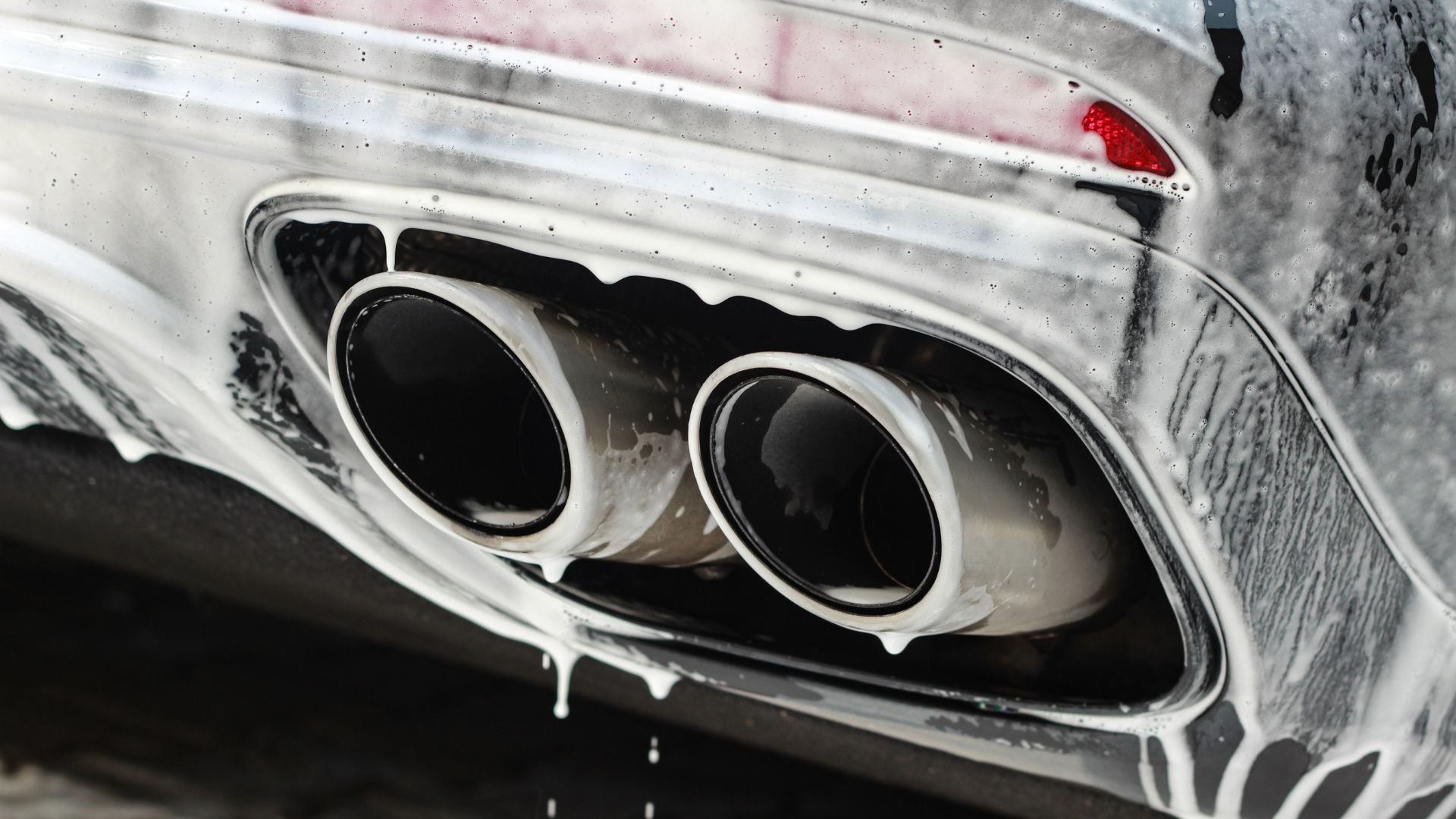 Dual exhaust pipes of a white car with water droplets and reflections