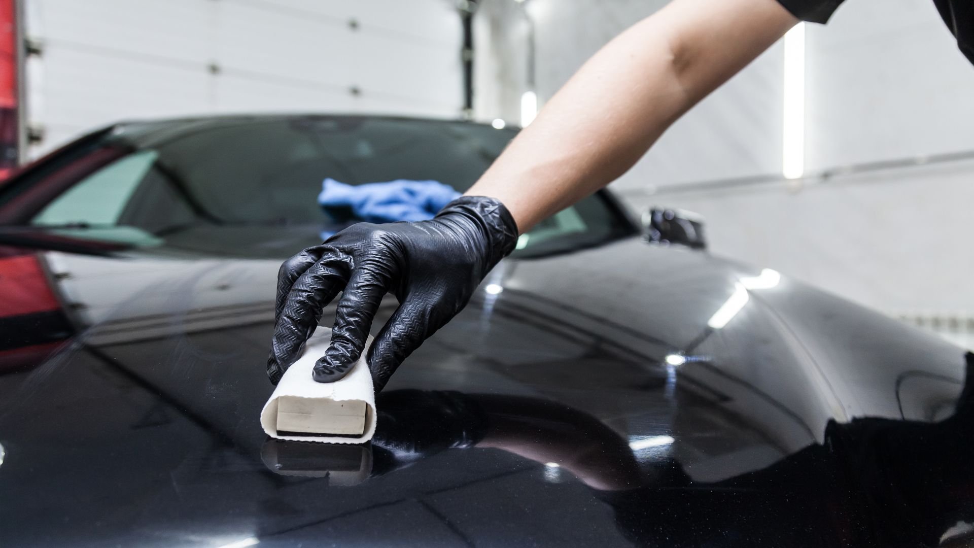 Gloved hand polishing a black car with a white cleaning tool