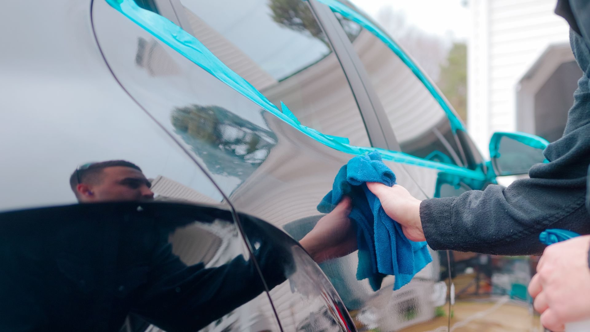 Hand wiping shiny black car with blue microfiber cloth