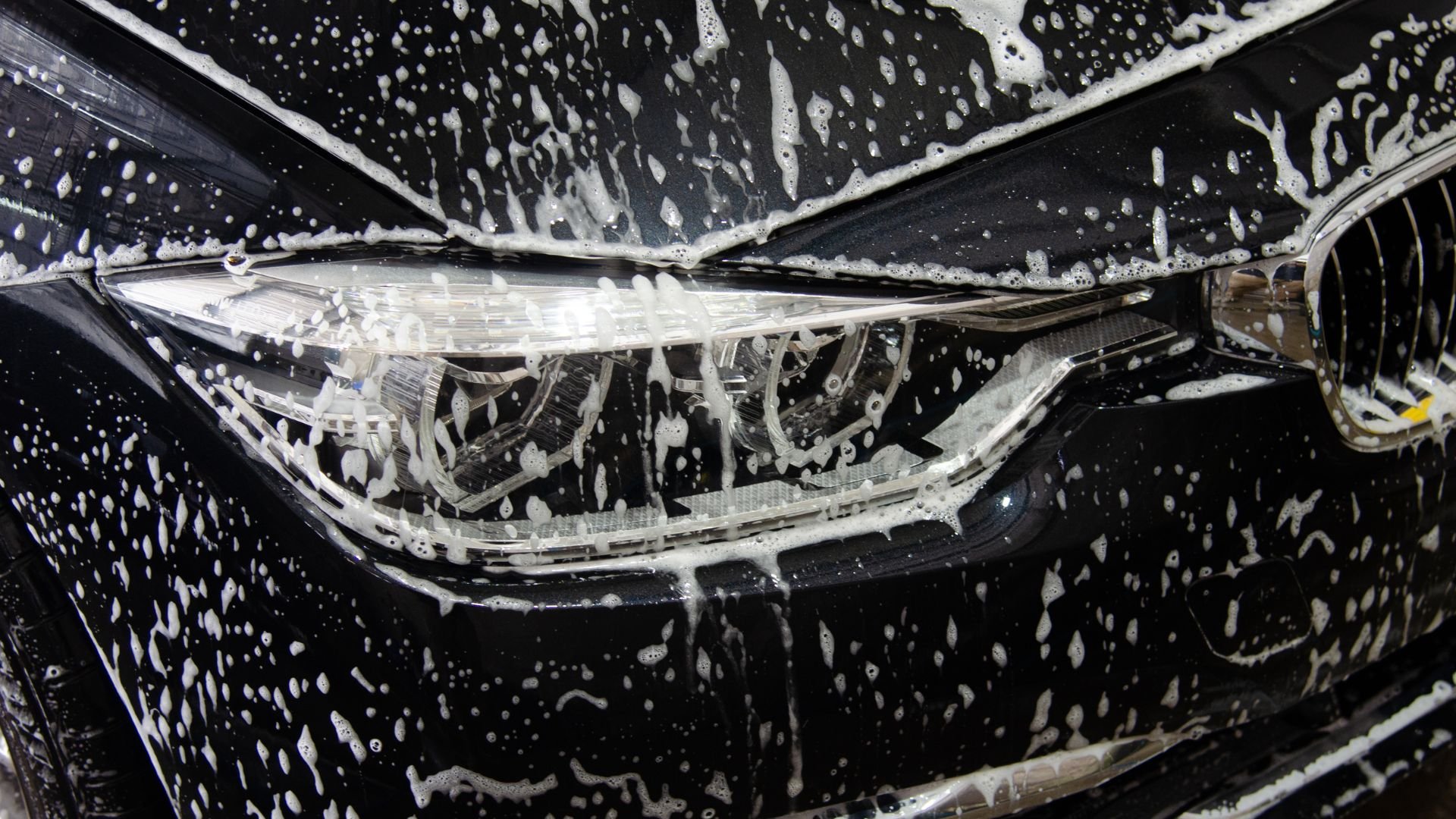 Car headlight covered in soap suds during a thorough car wash