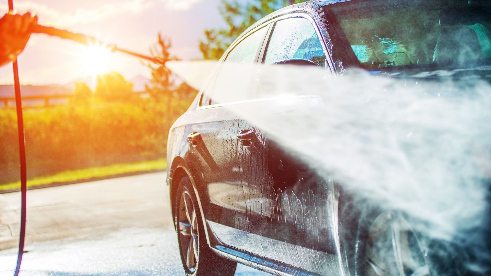 Car being washed with water spray at sunset near trees