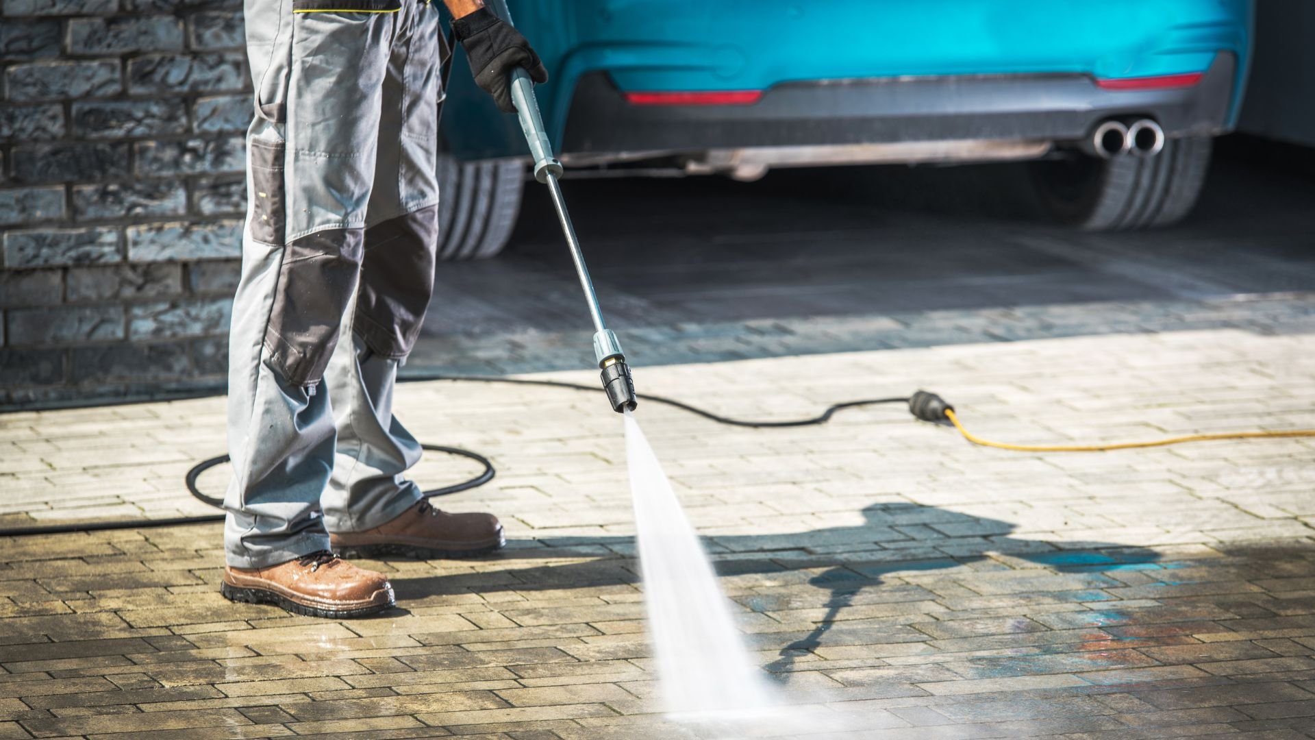 Cleaning brick pavement with high-pressure water jet near parked car
