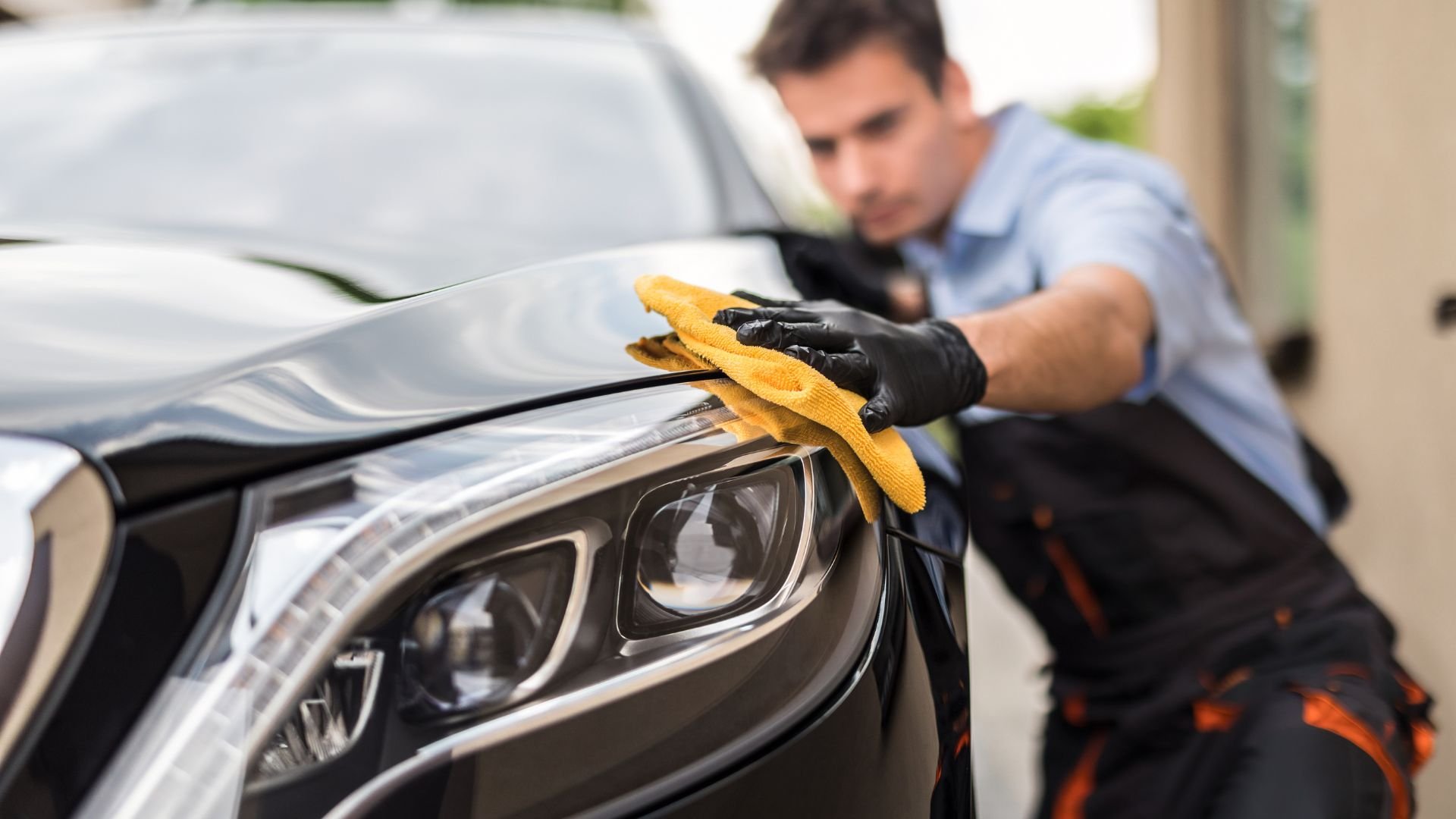 Car detailing professional cleaning a black car with a yellow microfiber cloth